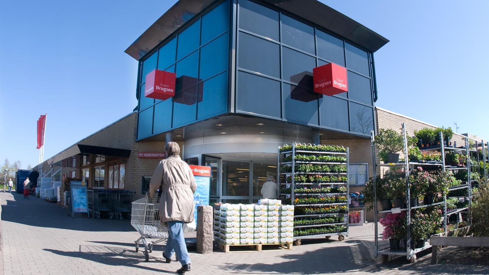 Woman pushes shopping cart towards entrance of supermarket SuperBrugsen